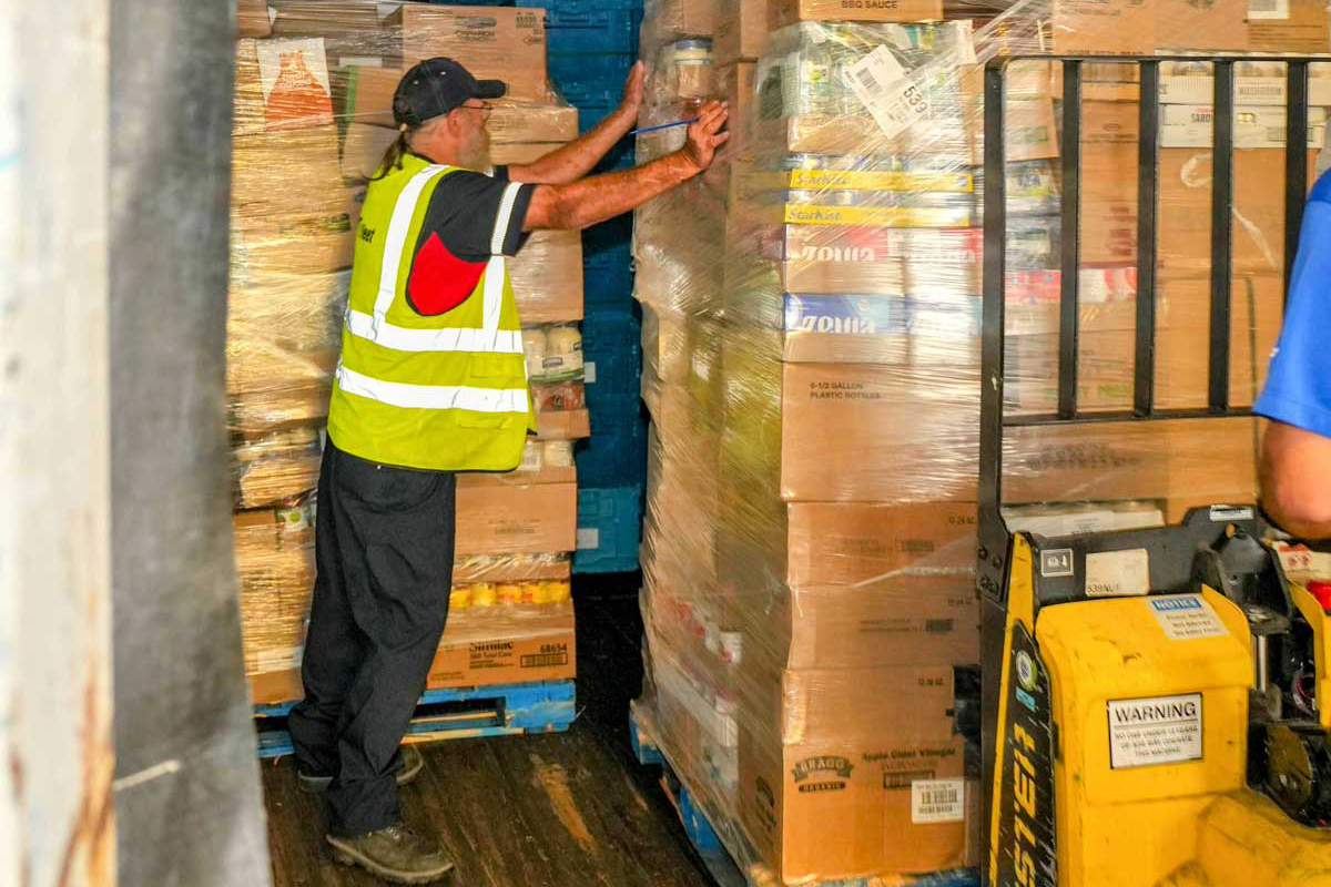 FirstFleet driver helping forklift operator unload grocery delivery from trailer